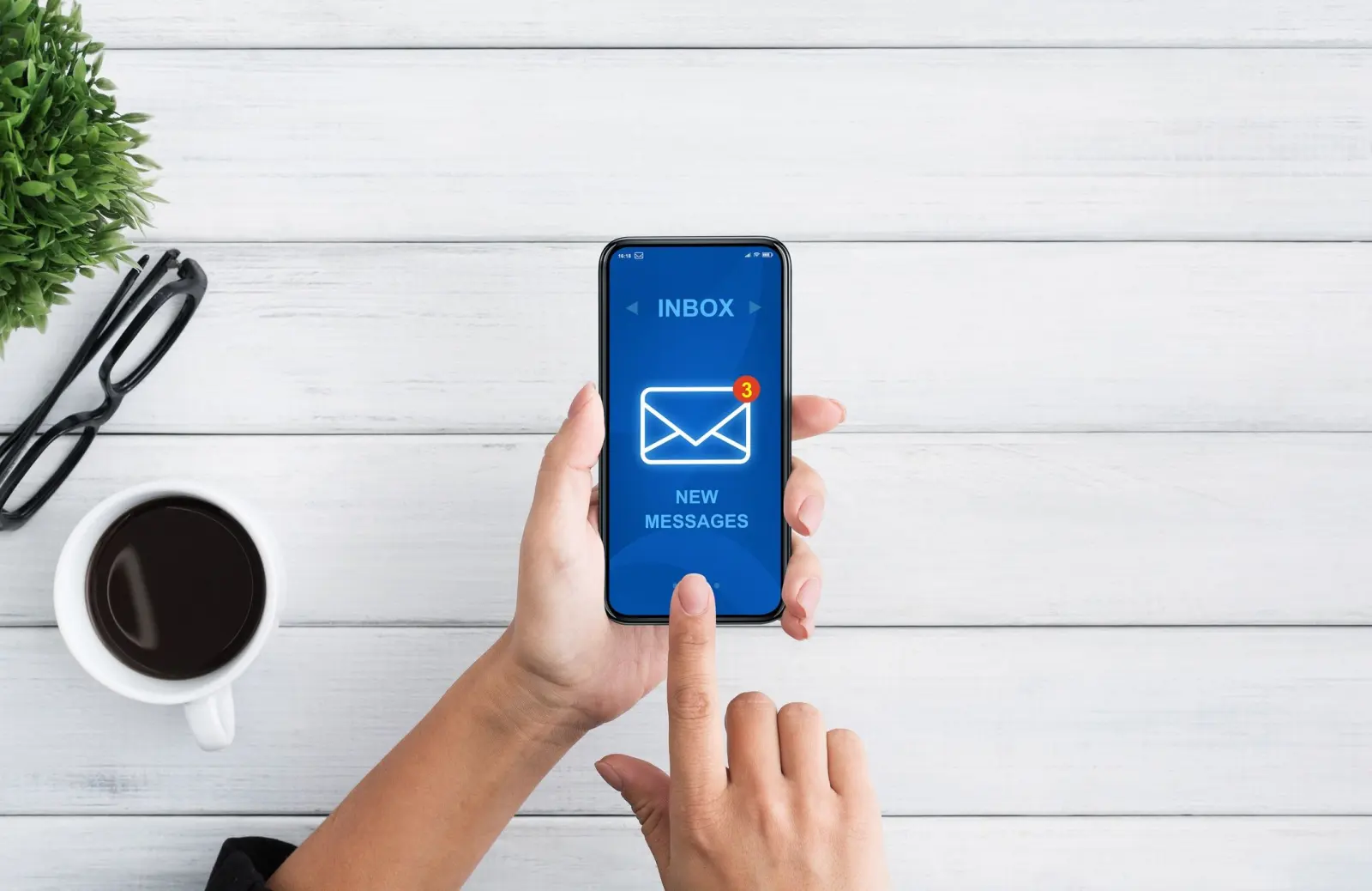 A persons hand holding a smartphone showing an email inbox.